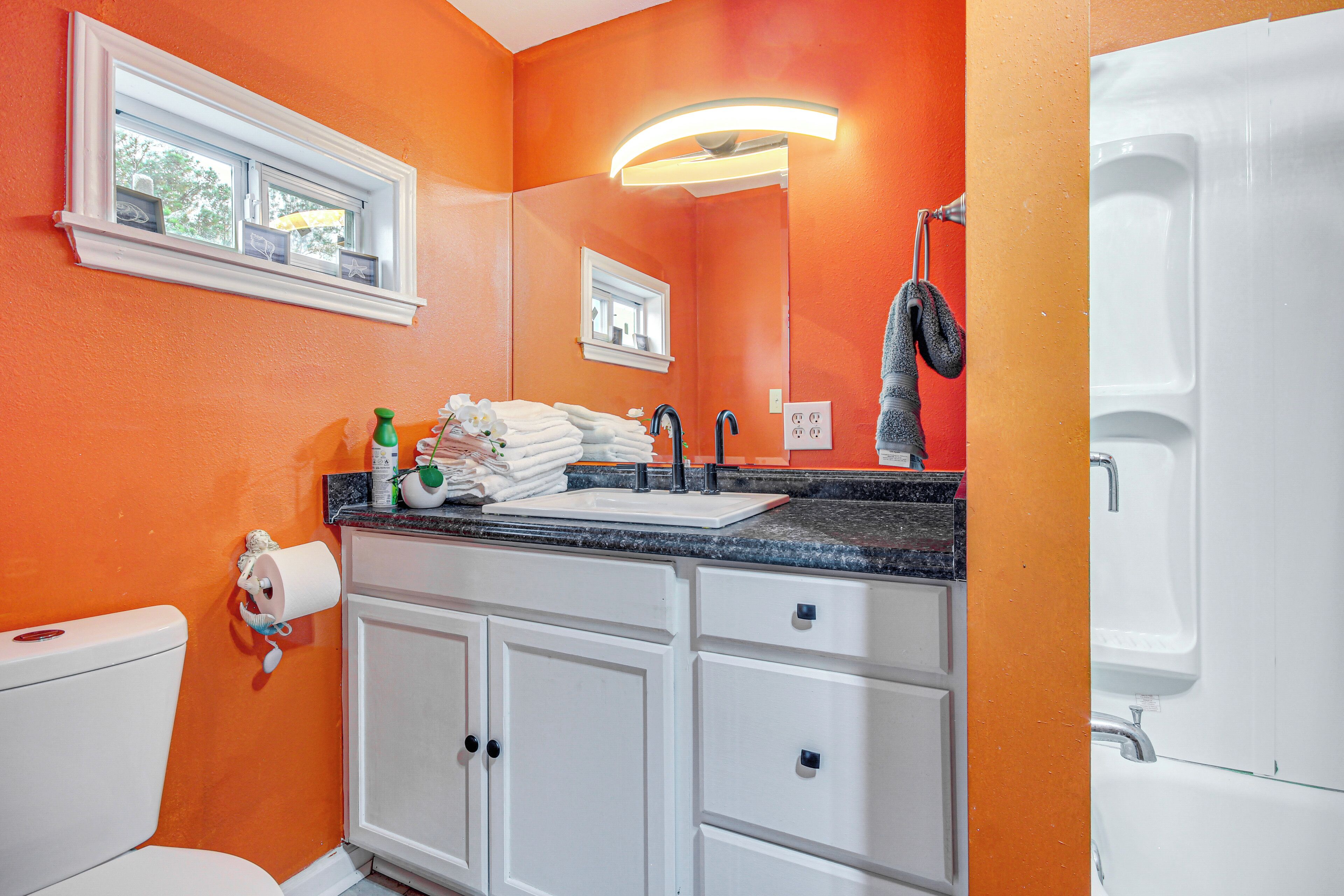 Ein Badezimmer mit orangefarbener Wand, weißen Schränken, einem Waschbecken mit schwarzem Wasserhahn und einem Handtuchhalter.