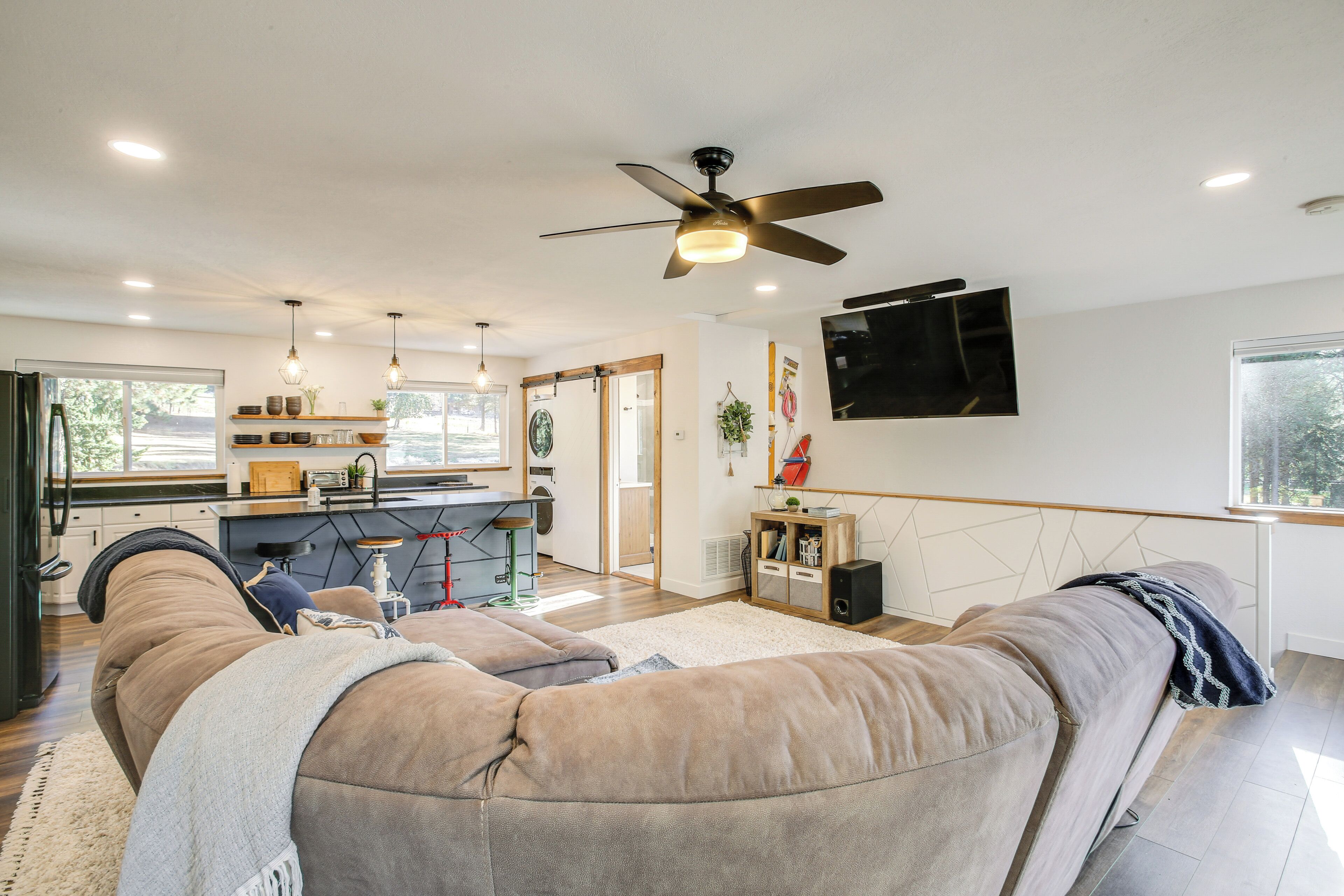 A modern living room with a large sectional sofa, a ceiling fan, and a kitchen in the background.