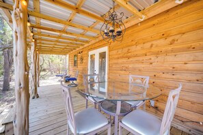 A wooden cabin with a glass table and chairs on a deck, a chandelier, and a door leading outside. - Happy Haven Hill Country Couples Cabin Retreat (Johnson City)