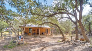 Ein rustikales Blockhaus mit Veranda, umgeben von Bäumen und Kiesgrundstück.