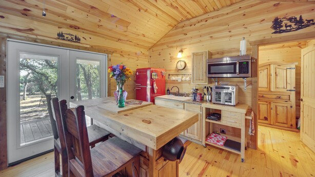 Ein Interieur einer Holzhütte mit Esstisch, Stühlen, Kühlschrank, Mikrowelle und Spüle.