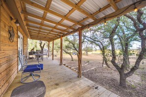 A covered wooden deck with outdoor furniture, a pergola, and a view of trees and landscape. - Happy Haven Hill Country Couples Cabin Retreat (Johnson City)