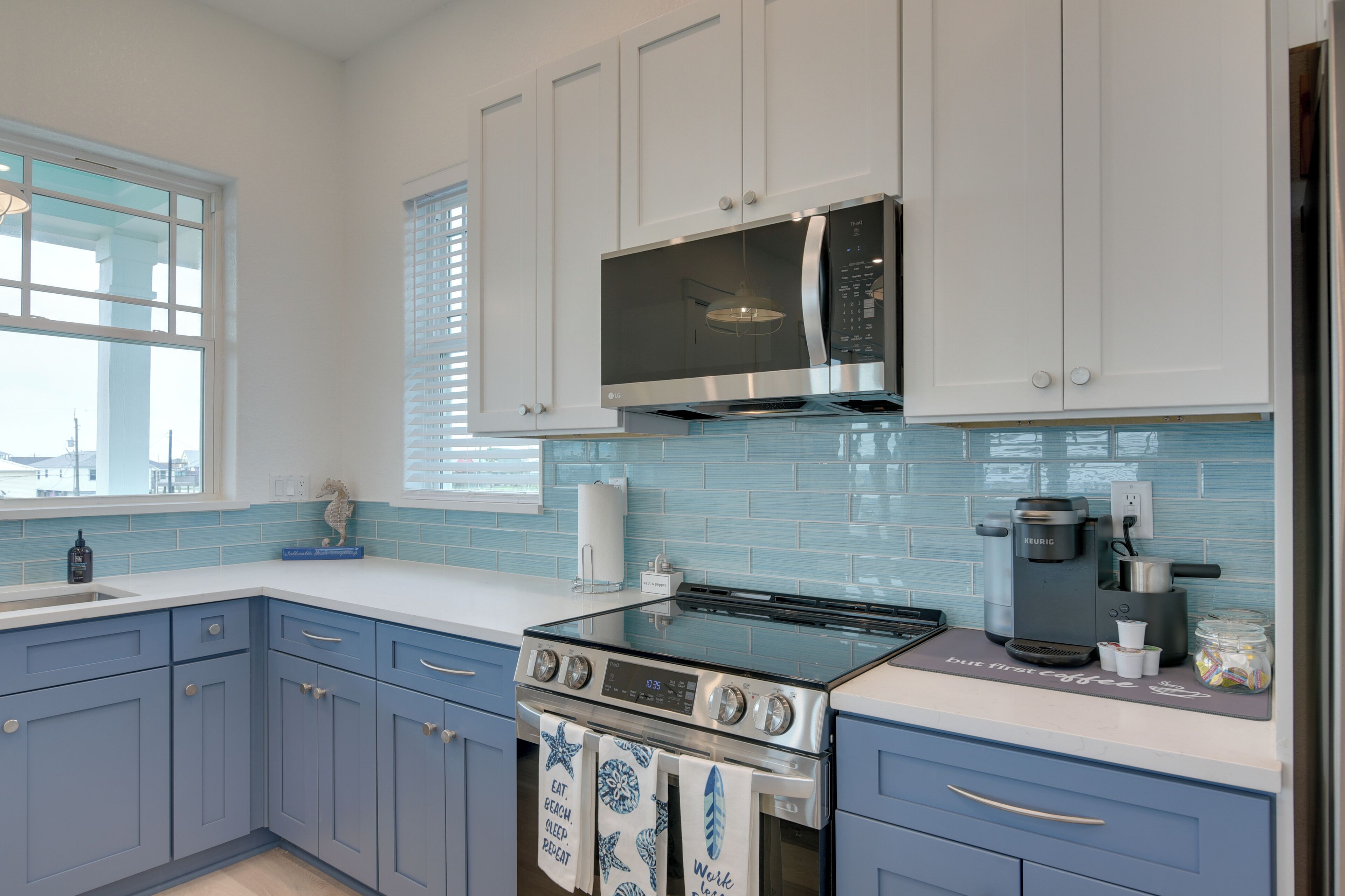 A modern kitchen with blue cabinets, a stainless steel stove, a microwave, and a coffee maker.