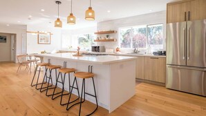 Une cuisine moderne dotée d’un îlot central, de tabourets de bar en bois, de luminaires suspendus et d’un réfrigérateur en acier inoxydable.