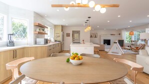 Une cuisine moderne avec des meubles blancs, un îlot central et un coin repas comprenant une table ronde et des chaises.
