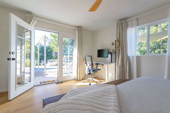A bedroom with a large bed, a desk with a chair, a television, and a sliding glass door leading to an outdoor area. - Modern Farmhouse on 1 Acre | Steps to Park | w/ Spa (Sebastopol)