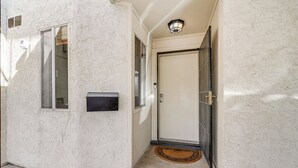 A narrow hallway with a white textured wall, a door with a black frame, and a small window. - Furnished Patio, Pool Access! Scottsdale Retreat (Scottsdale)