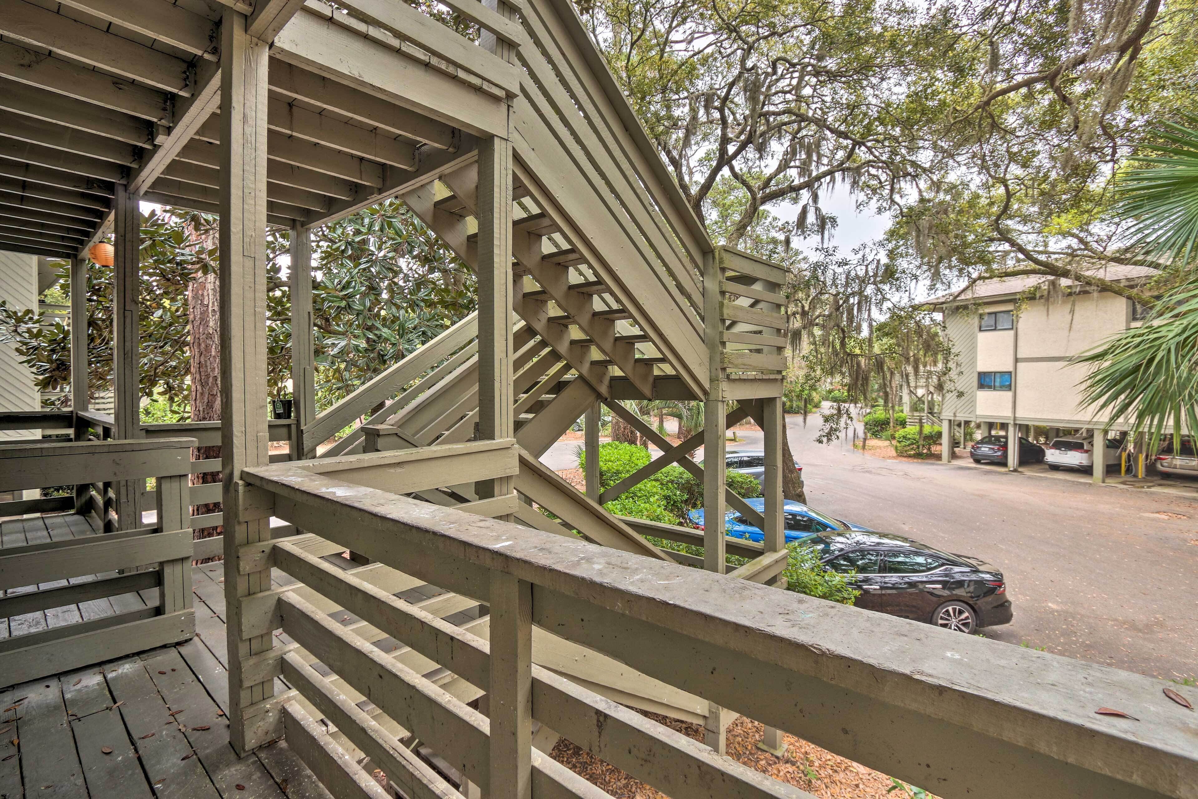 A wooden deck with a railing overlooking a parking area and a building.
