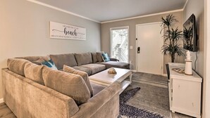 Un salon avec un canapé d’angle, une table basse, un téléviseur à écran plat, une plante en pot et un tableau accroché au mur.