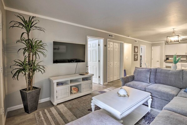 A living room with a grey sofa, a white coffee table, a TV on the wall, a potted plant, and a white cabinet. - < 1 Mi to Beach: Hilton Head Condo w/ Pool Access! (Hilton Head Island)