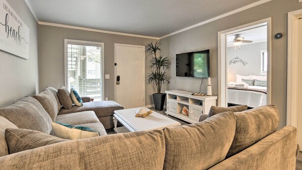 Un salon avec un canapé beige, une table basse blanche, une plante en pot et un téléviseur à écran plat fixé au mur.