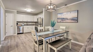 Una cocina moderna con armarios blancos, electrodomésticos de acero inoxidable y un comedor con mesa y sillas.