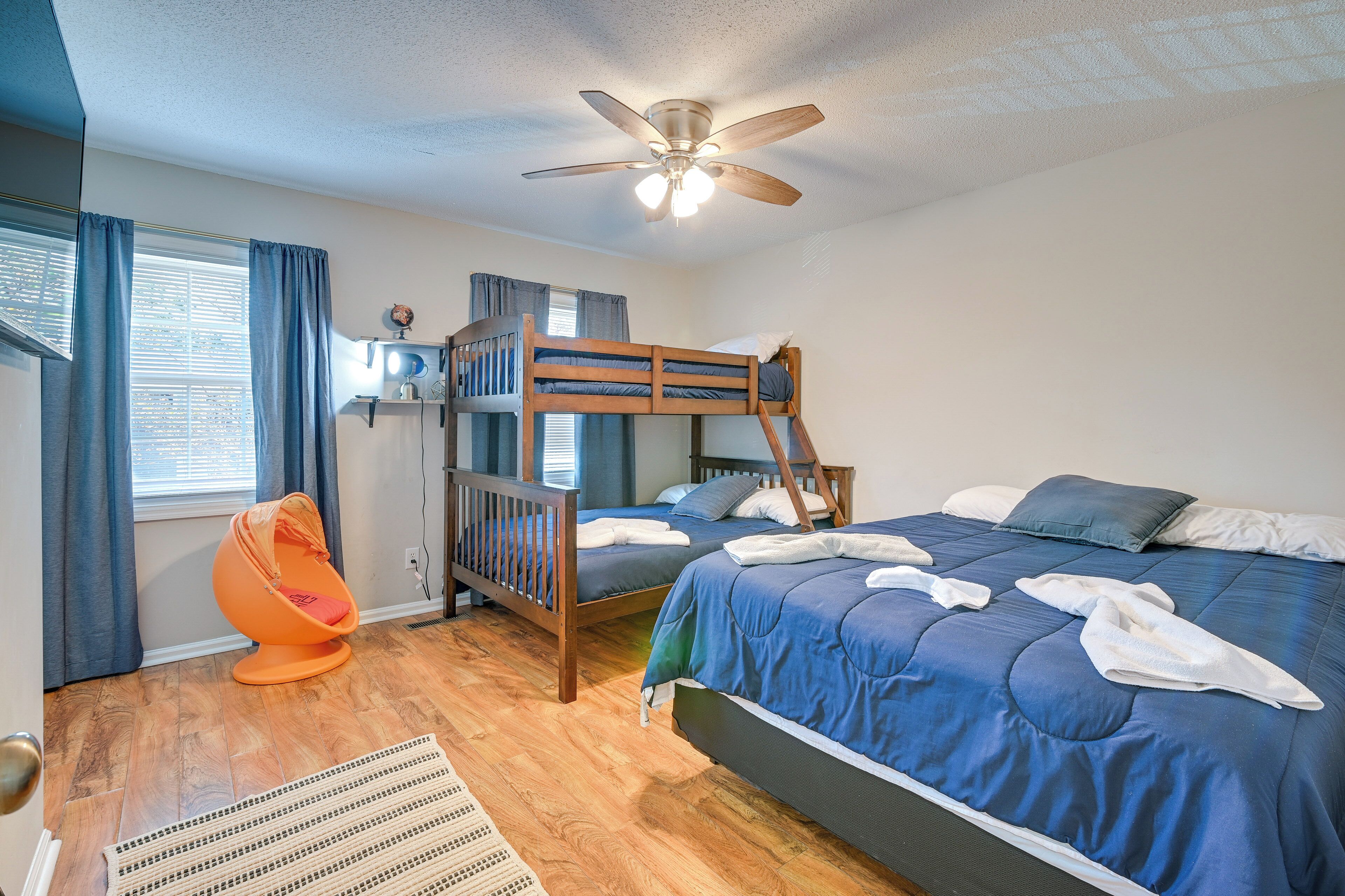 A bedroom with bunk beds, a ceiling fan, a desk lamp, and a window with curtains.