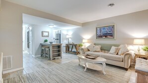 A spacious living room with a sofa, coffee table, and lamps. There is a kitchen area in the background with a refrigerator and a dining table. - Walk to Ocean - Townhome w/ Patio in Myrtle Beach! (Myrtle Beach)