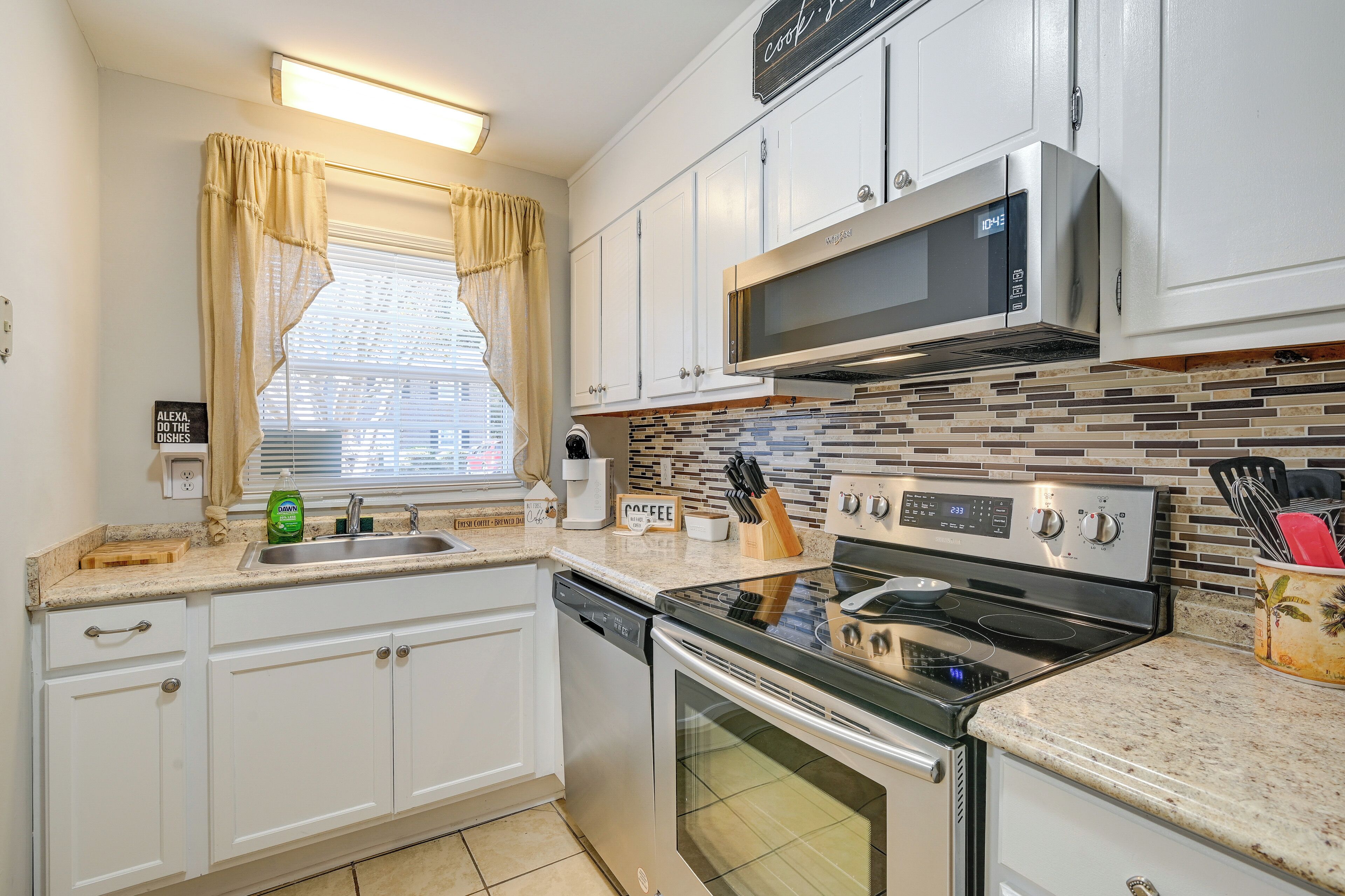 A modern kitchen with white cabinets, a stainless steel microwave, an oven, and a dishwasher.