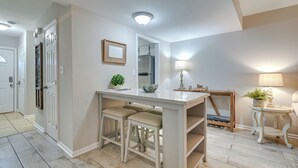 A kitchen with a white countertop, two stools, a small plant, and a wooden table with a lamp. - Walk to Ocean - Townhome w/ Patio in Myrtle Beach! (Myrtle Beach)
