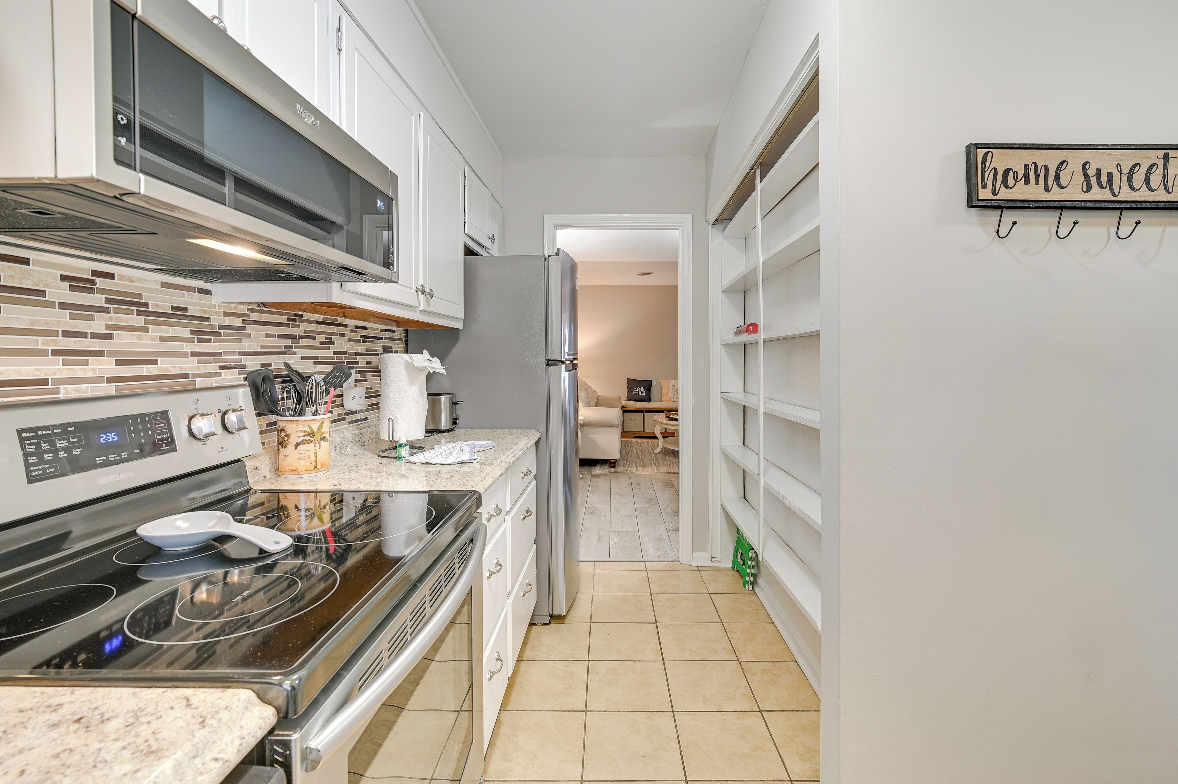 A modern kitchen with white cabinets, a stainless steel refrigerator, and a digital clock displaying 2:35.
