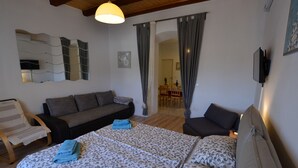 A cozy room with a sofa, a bed with patterned bedding, a chair, and a dining area in the background.