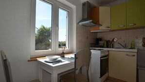 A compact kitchen with a window, a stove, a sink, and a chair.