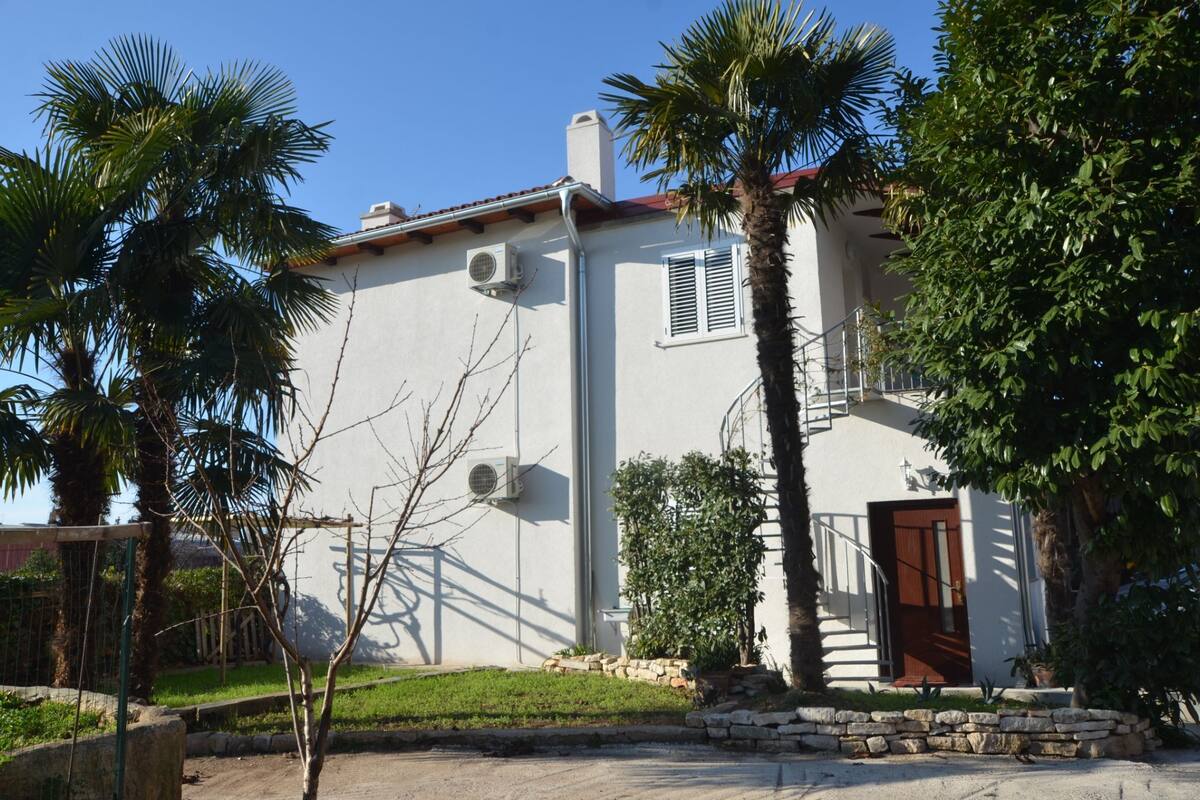 A two-story building with a white exterior, air conditioning units, a red-tiled roof, and a wooden door.