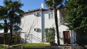 A two-story building with a white exterior, air conditioning units, a red-tiled roof, and a wooden door.