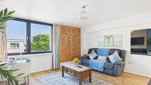 A living room with a glass table, a sofa with cushions, a coffee table with a vase, and a painting on the wall. - Harbour Hideaway - 1 Bedroom Apartment - Saundersfoot (Saundersfoot)