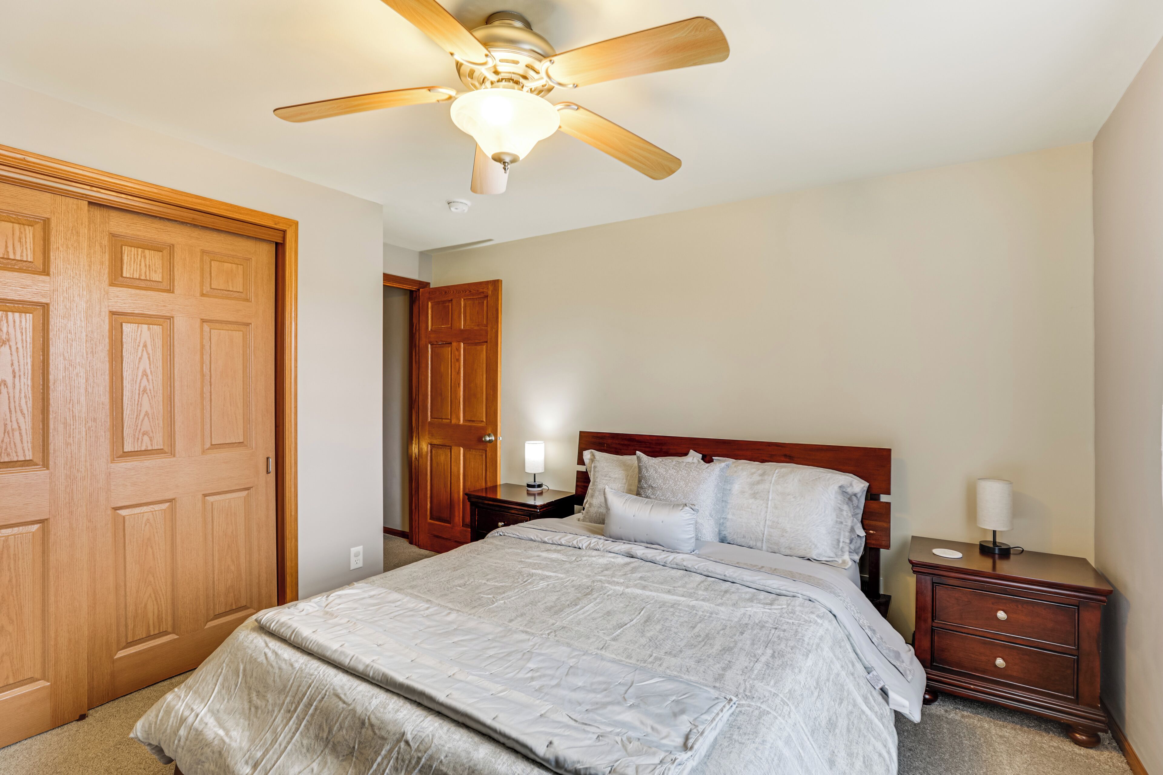 Un dormitorio con cama, cabecera de madera, mesita de noche y ventilador de techo.