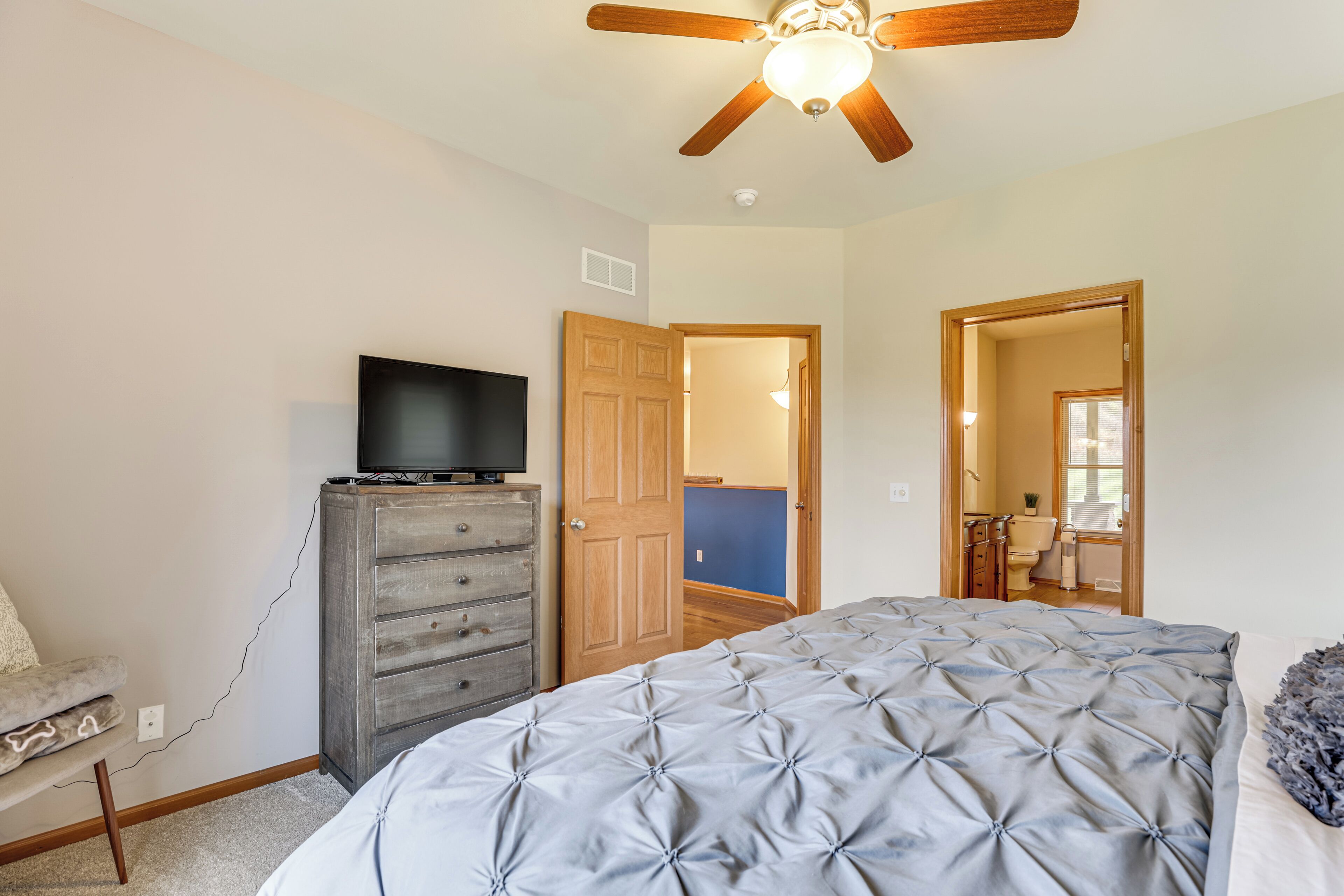 A bedroom with a bed, a dresser, a television on the dresser, and a ceiling fan.