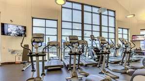 Une salle de sport équipée de plusieurs tapis de course et de plusieurs appareils elliptiques, dotée de grandes fenêtres et d’un téléviseur fixé au mur.