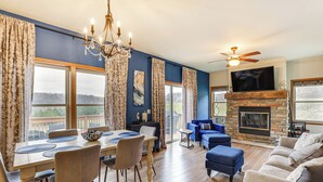 Un salon spacieux avec une cheminée, un coin repas avec une grande table et des chaises, et un coin salon confortable avec des canapés et des poufs.