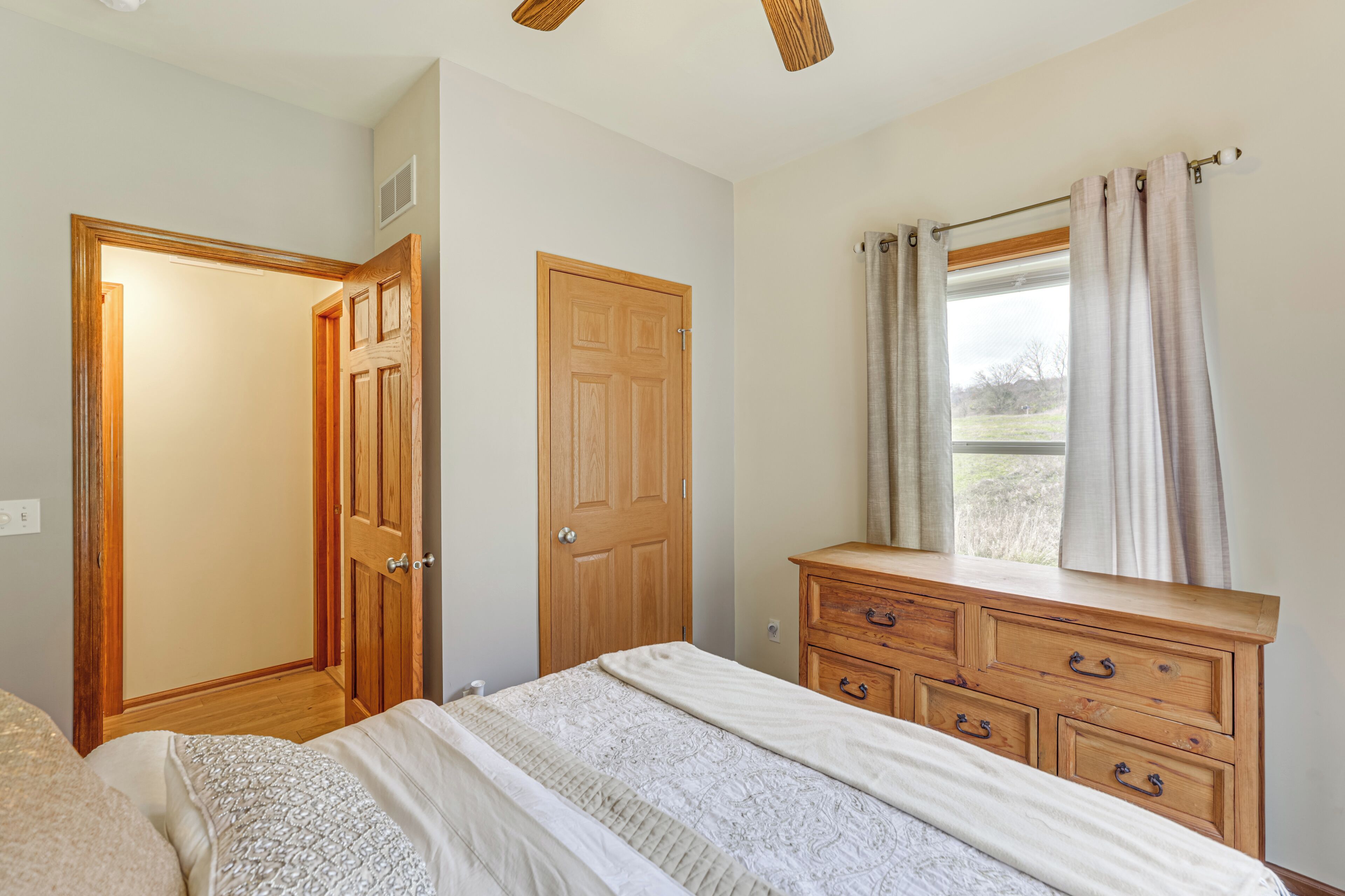 A bedroom with a bed, wooden dresser, and a window with curtains.