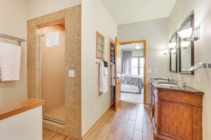 Un baño con ducha, tocador con espejo y una puerta que da a un dormitorio.