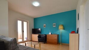 A living room with a sofa, a TV, a desk, a lamp, and a wardrobe. - Spacious Apartment With Loggia (Rovinj)