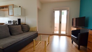 A modern living room with a sofa, a glass coffee table, a television, and a sliding glass door leading to a balcony. - Spacious Apartment With Loggia (Rovinj)