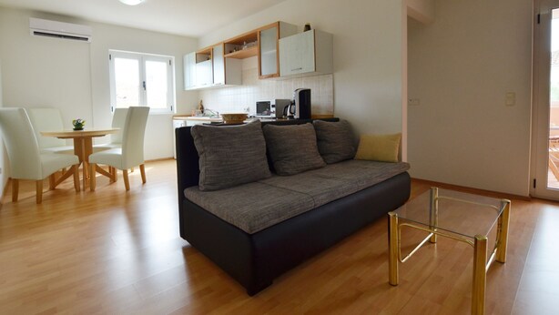 A modern living room with a sofa, a dining table with chairs, and a kitchen area with cabinets and appliances. - Spacious Apartment With Loggia (Rovinj)