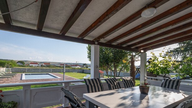 Un patio exterior cubierto con piscina, zona de estar y vistas del paisaje circundante.