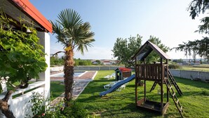 A backyard with a wooden playhouse, a palm tree, and a grapevine. - House Rose With Garden and Pool (Razanac)