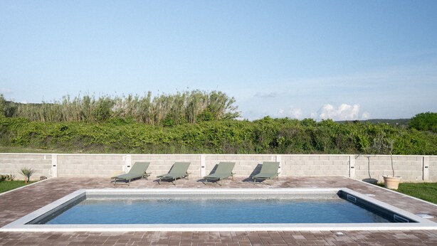 A rectangular swimming pool with four lounge chairs aligned along its length. - House Rose With Garden and Pool (Razanac)