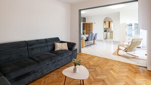 A modern living room with a dark sofa, a round coffee table, and a view into a kitchen and dining area. - House Rose With Garden and Pool (Razanac)