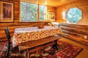 A rustic wooden cabin interior with a dining table, chairs, and a bench.