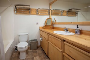 A bathroom with a toilet, sink, mirror, towel racks, and a trash can.