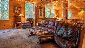 A cozy cabin interior with a leather sofa, a wooden coffee table, and a bookshelf.