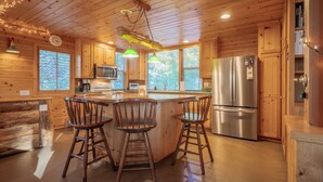 A wooden cabin kitchen with a central island, bar stools, a refrigerator, and a microwave.