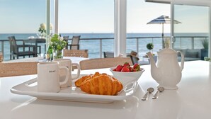 Un plateau de petit-déjeuner avec des croissants, un bol de fraises, deux tasses et une théière, le tout posé sur une table offrant une vue sur la mer.