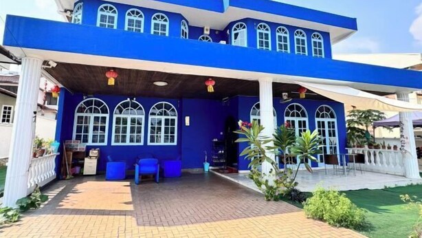 Un edificio de dos plantas con fachada azul y detalles blancos, que cuenta con ventanas arqueadas y una zona de entrada cubierta con asientos.