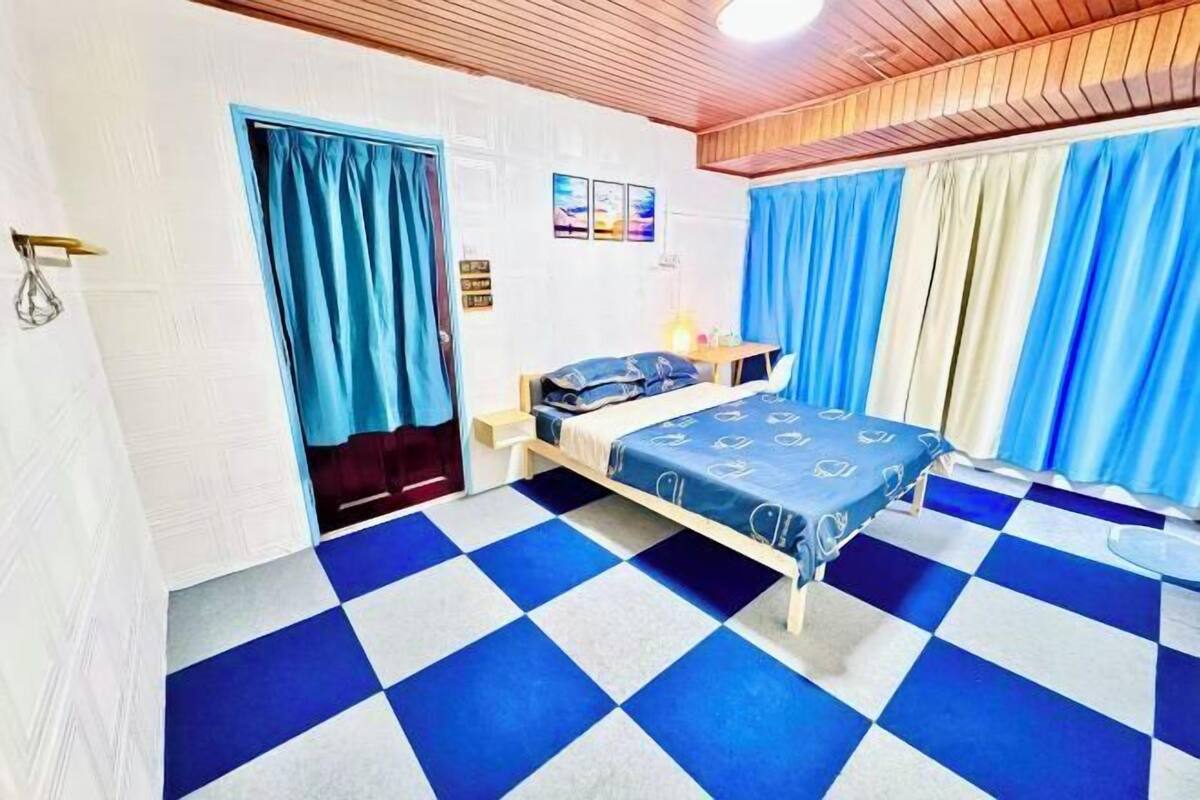 A room with a checkered floor, a bed with a patterned bedspread, a nightstand, and curtains.