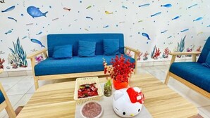 Una habitación con un sofá azul, una mesa de centro de madera con un adorno de Hello Kitty y una pared con estampado de peces.