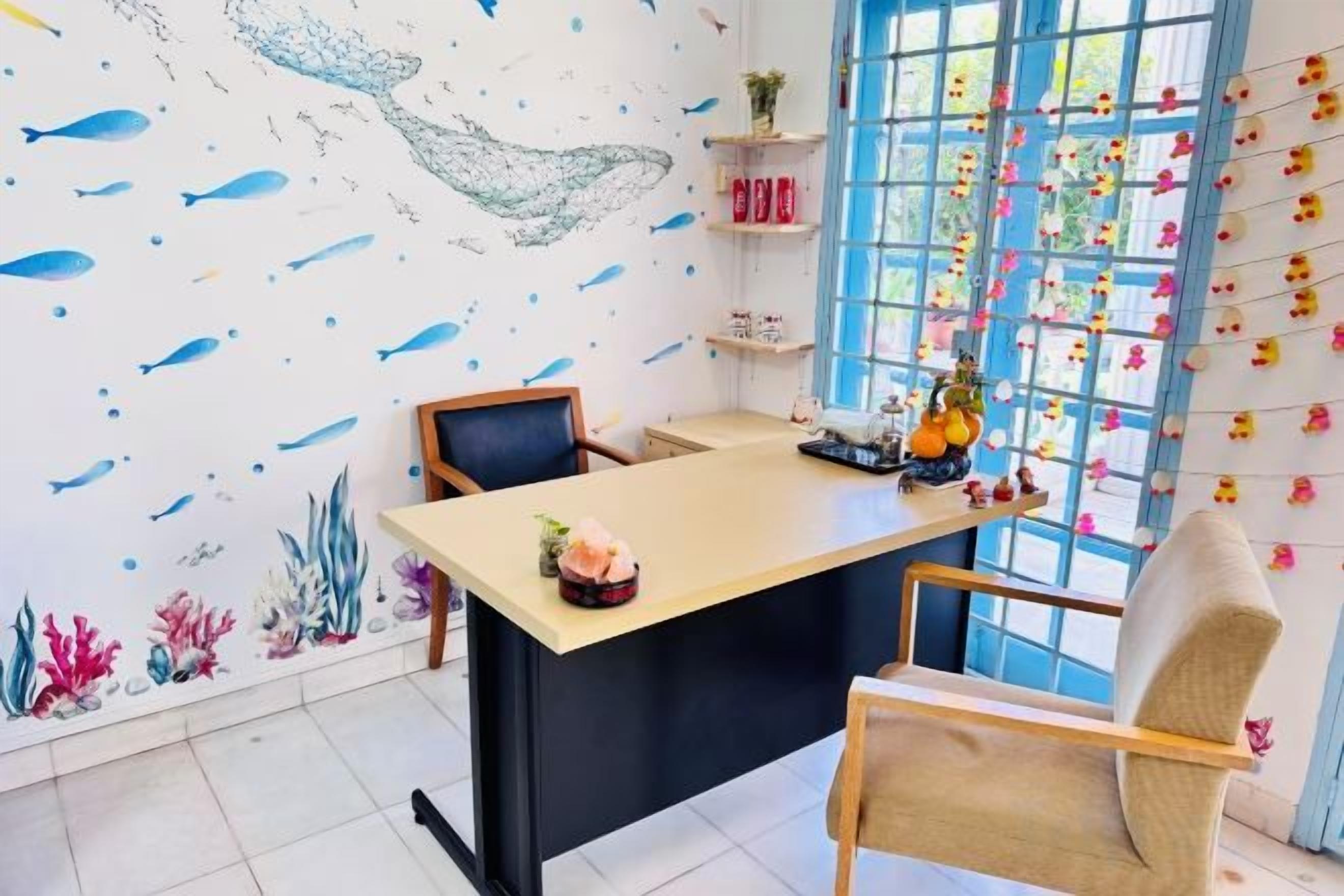 A room with a desk, chairs, a window with a view, and a wall with a fish pattern.