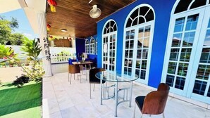 Un patio exterior con una mesa y sillas de vidrio, rodeado de paredes azules y amplias ventanas arqueadas.