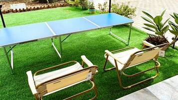 A ping pong table with two chairs on artificial grass.